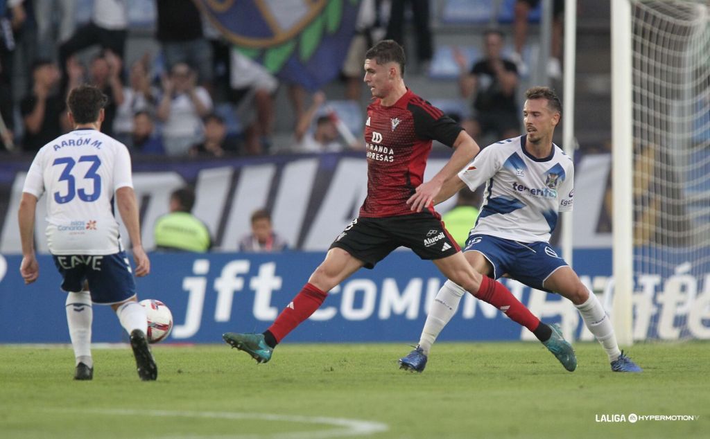 Jugador del CD Mirandés da un pase entre dos jugadores blanquiazules (CD Mirándes)