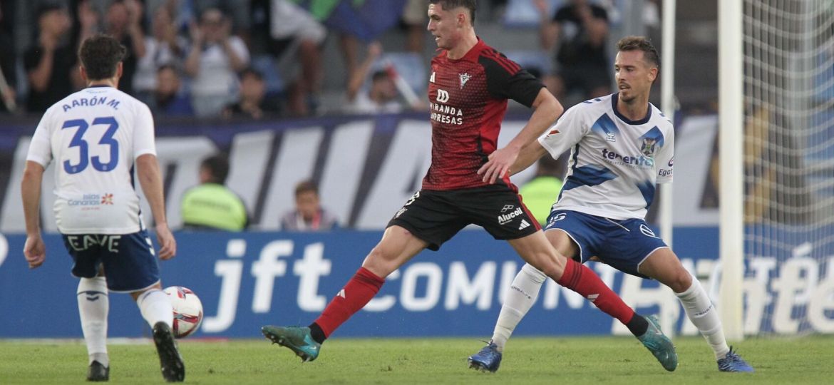 Jugador del CD Mirandés da un pase entre dos jugadores blanquiazules (CD Mirándes)