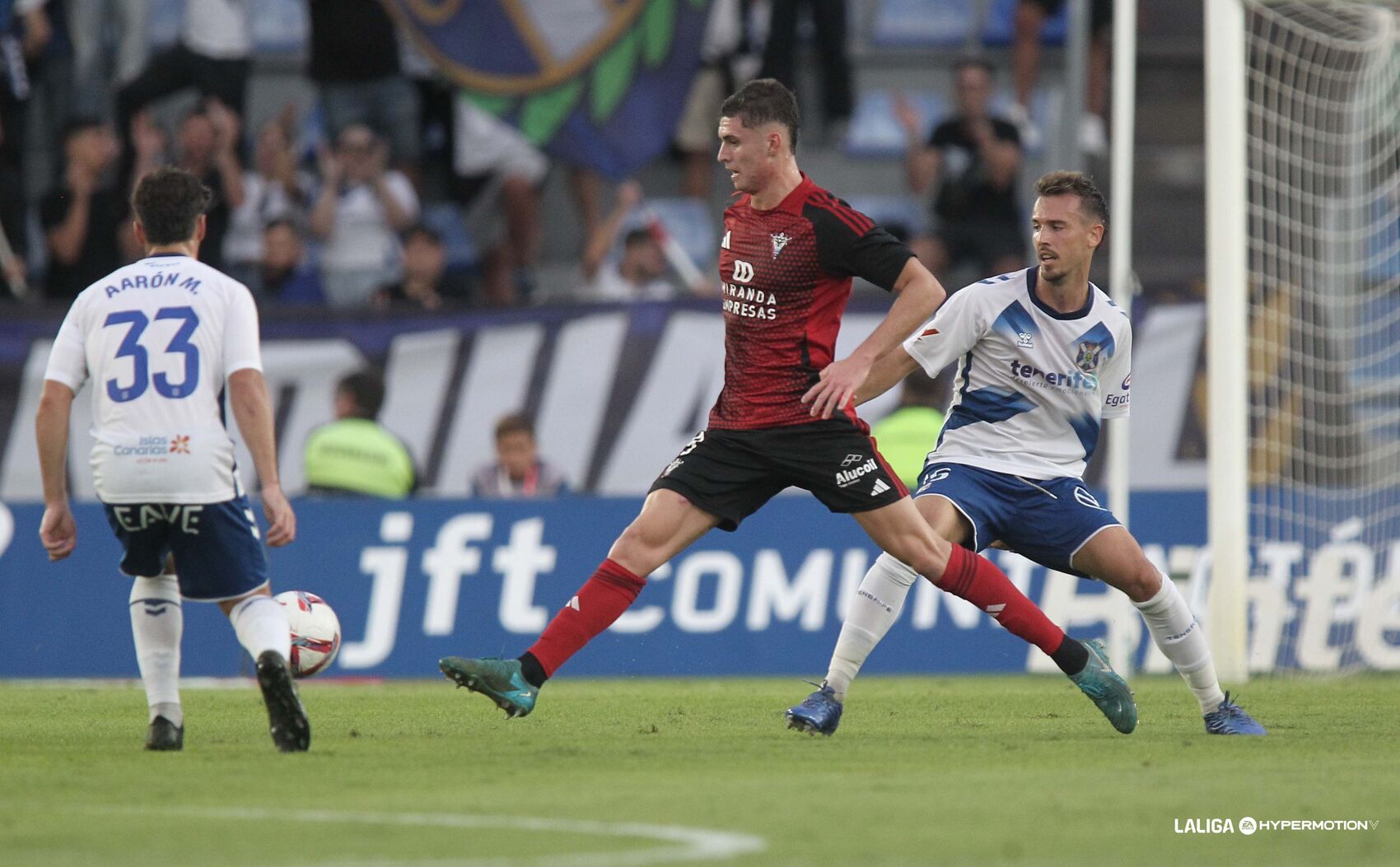 Jugador del CD Mirandés da un pase entre dos jugadores blanquiazules (CD Mirándes)